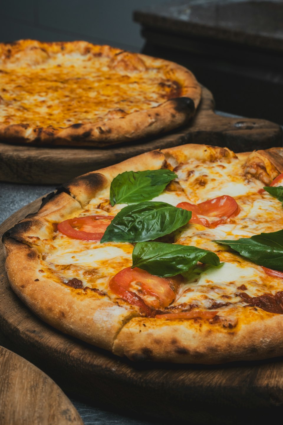 Due pizze con pomodoro, mozzarella e basilico su taglieri di legno.