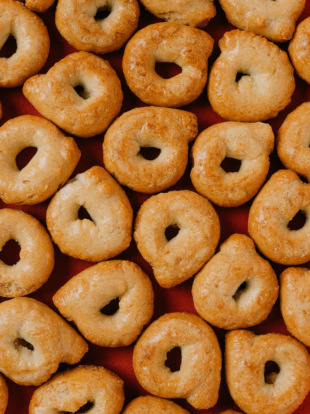 Taralli dorati disposti su una superficie rossa.