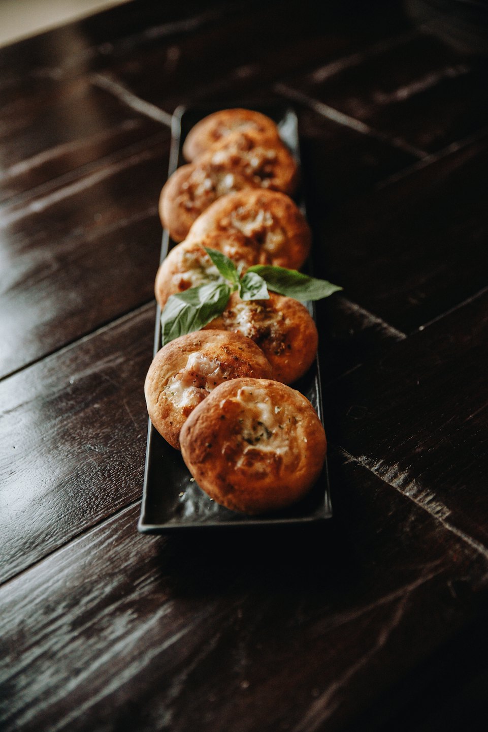 Sei mini pizze condite con basilico su un vassoio di legno.